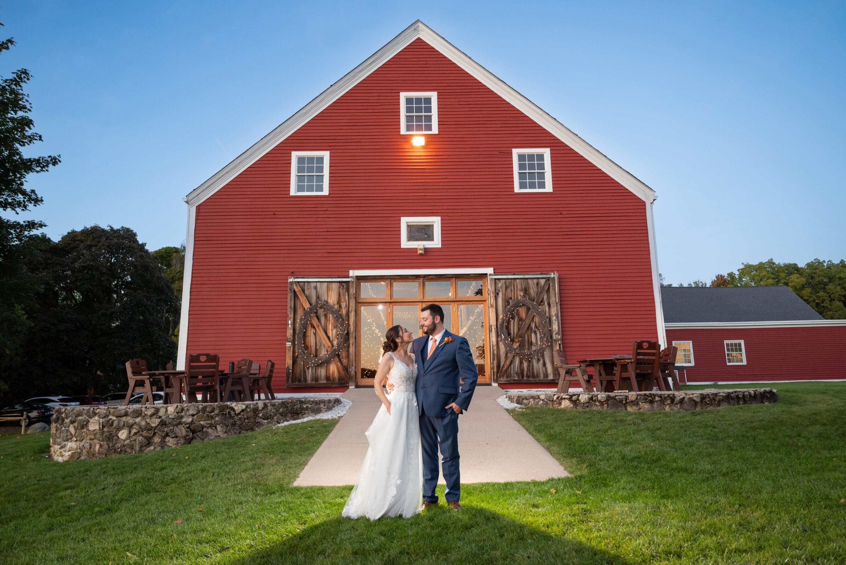Bride and groom posing in front of a red barn at sunset.