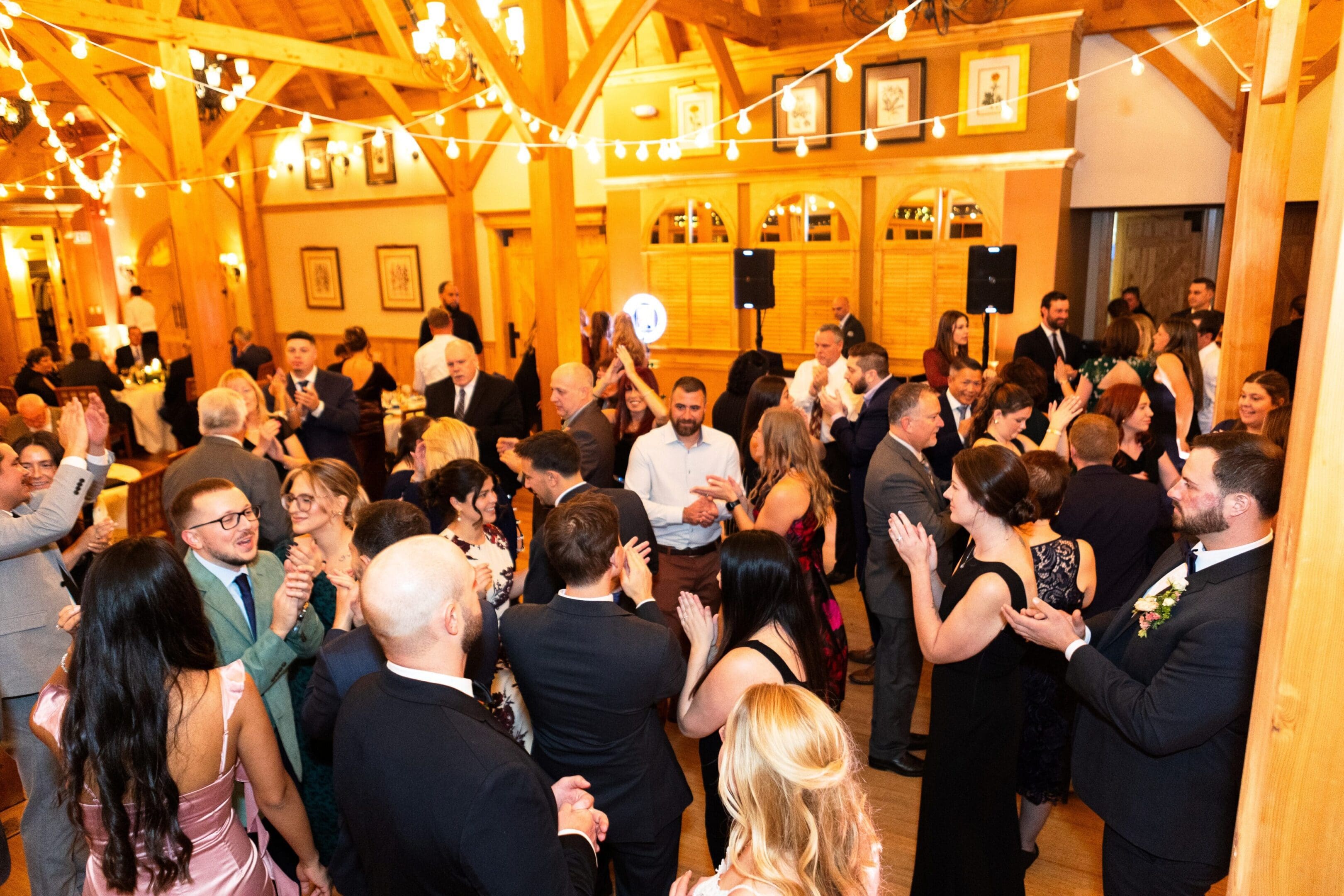 A crowded indoor party with people socializing and dancing under warm lighting.